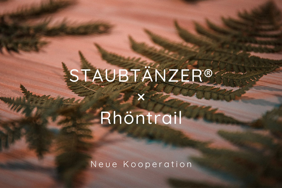 Ein Farn, liegend auf dem Tisch mit dem Text "STAUBTÄNZER® x Rhöntrail – Neue Kooperation"