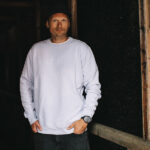 Ein Mann in einem dicken parma-farbenem Sweater schaut in die Kamera