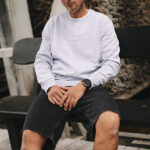 Ein Mann in einem dicken parma-farbenem Sweater sitzt auf einer Bank