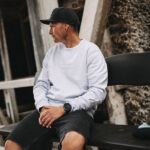 Ein Mann in einem dicken parma-farbenem Sweater sitzt auf einer Bank